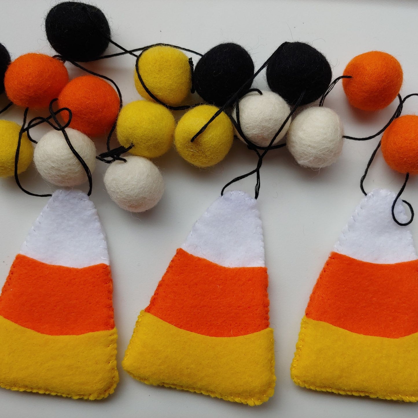 Handcrafted Candy Corn Felt Garland featuring yellow, orange, white, and black felt candy corn pieces with felt balls. A festive Halloween and fall decoration.