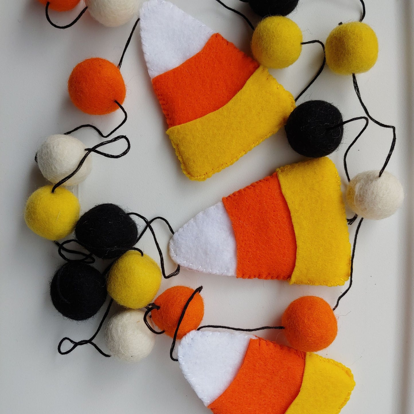 Handcrafted Candy Corn Felt Garland featuring yellow, orange, white, and black felt candy corn pieces with felt balls. A festive Halloween and fall decoration.
