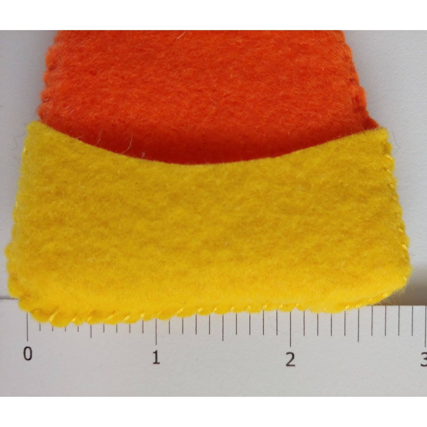 Handcrafted Candy Corn Felt Garland featuring yellow, orange, white, and black felt candy corn pieces with felt balls. Ruler at base of candy corn piece. A festive Halloween and fall decoration.
