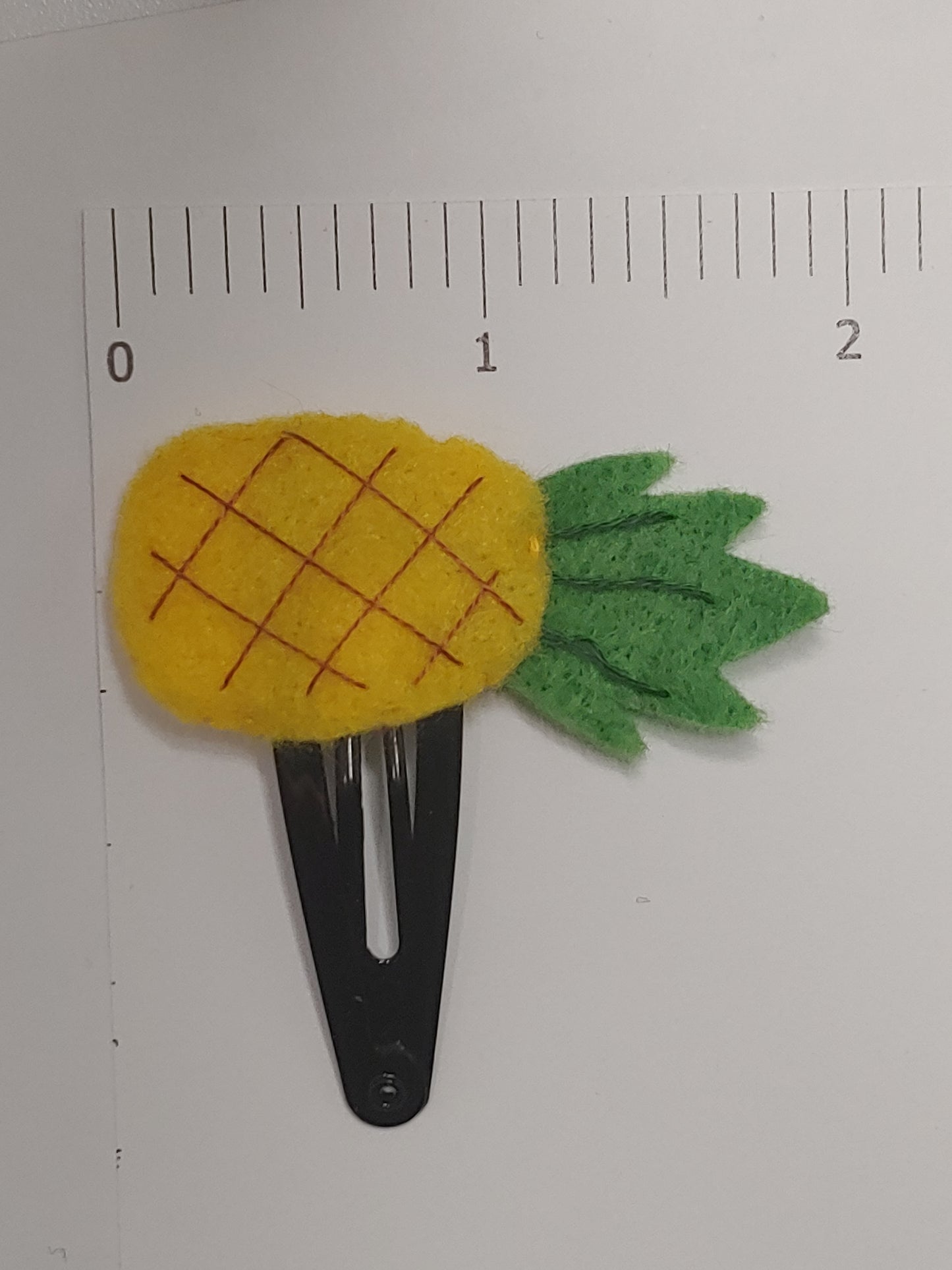 Handmade felt fruit hair clip featuring Pineapple design on metal snap clips. Positioned next to ruler.