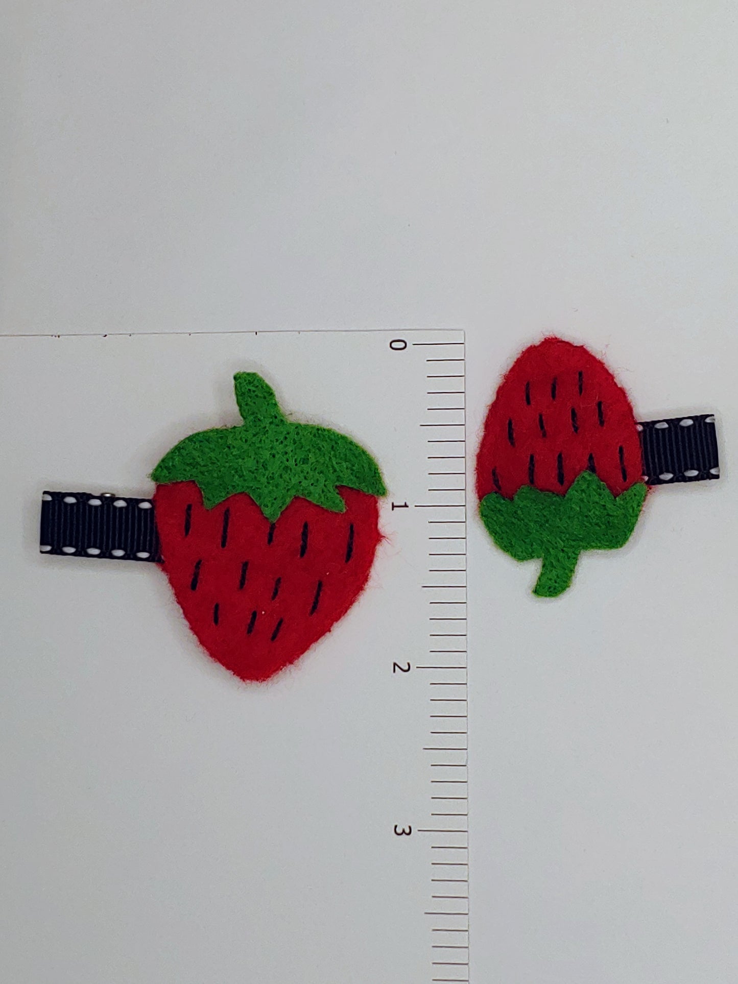 Handmade Mommy & Me Strawberry Hair Clip Set featuring vibrant felt strawberries on alligator clips. A charming, matching accessory for moms and daughters. Placed next to ruler.