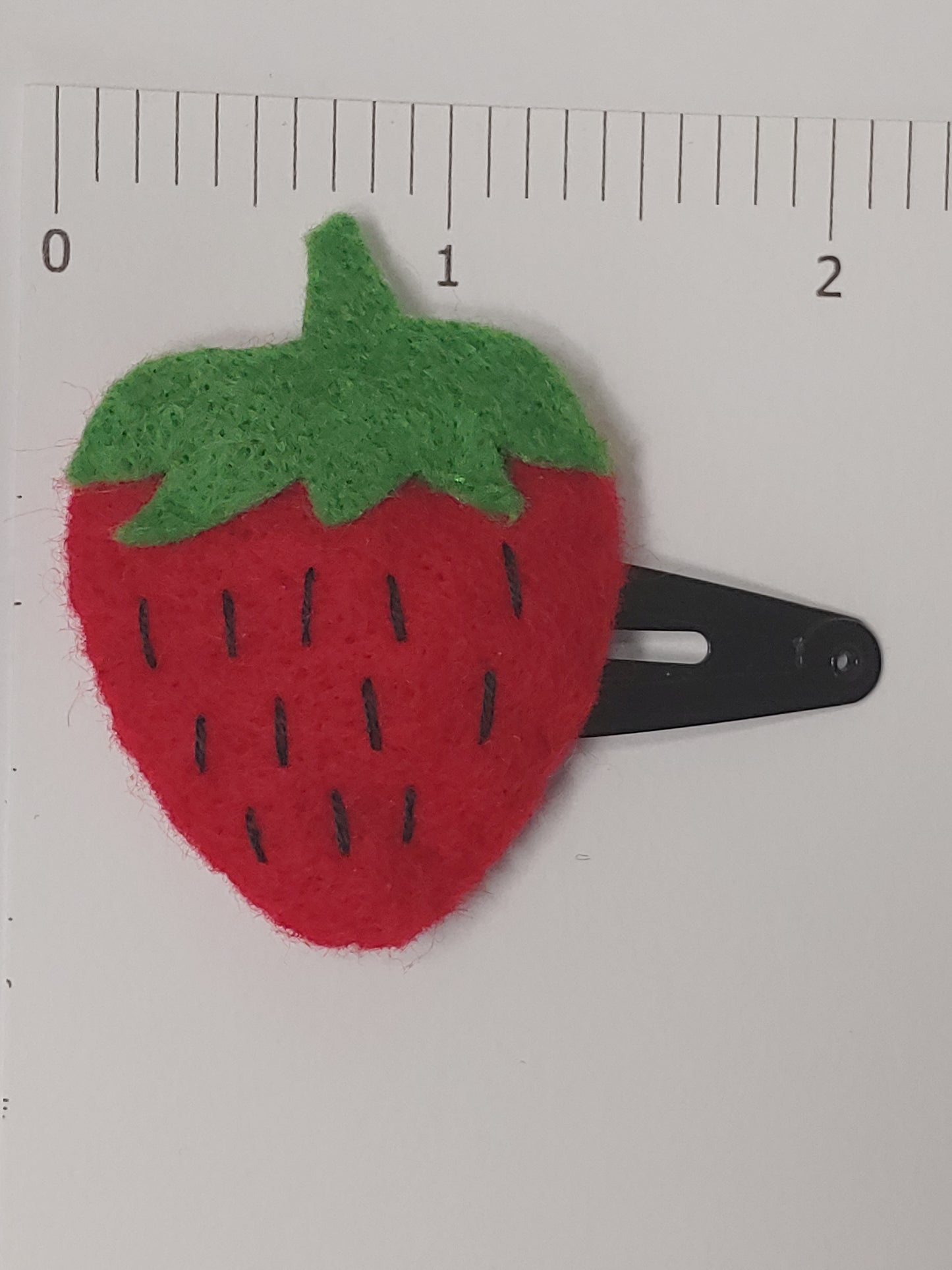 Handmade felt fruit hair clip featuring Strawberry design on metal snap clips. Positioned next to ruler.