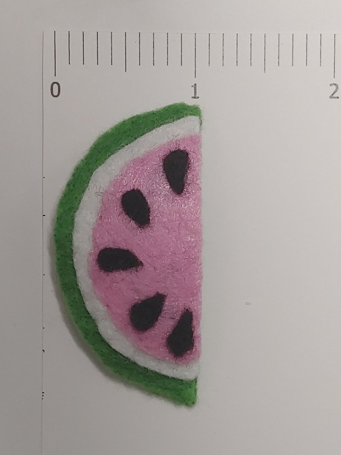 Handmade felt fruit hair clip featuring Watermelon Slice design on metal snap clips. Positioned next to ruler.
