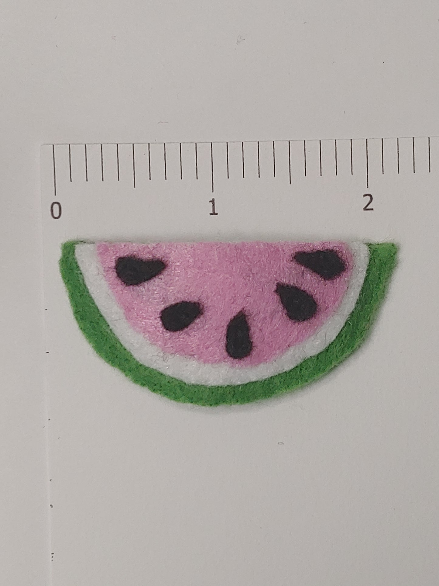 Handmade felt fruit hair clip featuring Watermelon Slice design on metal snap clips. Positioned next to ruler.