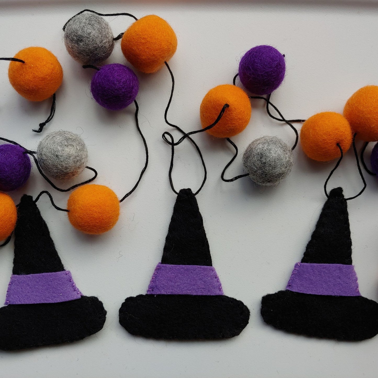 Handcrafted Witches Hat Felt Garland featuring purple, orange, black, and gray felt hats and felt balls. A whimsical Halloween decoration.