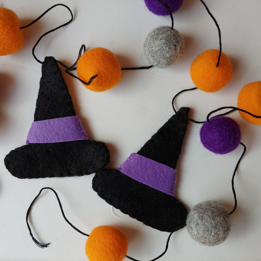 Handcrafted Witches Hat Felt Garland featuring purple, orange, black, and gray felt hats and felt balls. A whimsical Halloween decoration.