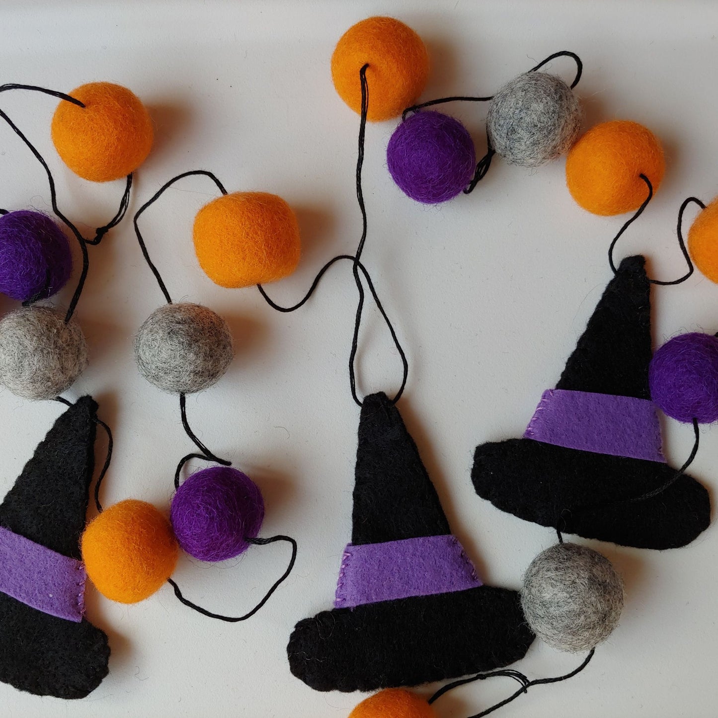 Handcrafted Witches Hat Felt Garland featuring purple, orange, black, and gray felt hats and felt balls. A whimsical Halloween decoration.