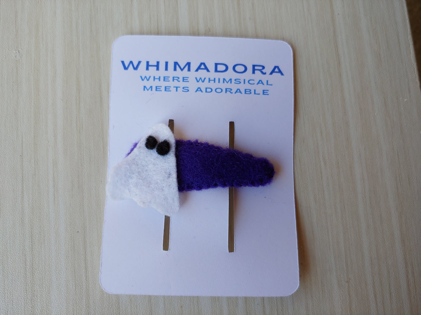 Handcrafted Ghost Felt Hair Clip featuring white felt with black details on a secure purple snap clip. A fun and festive Halloween accessory.