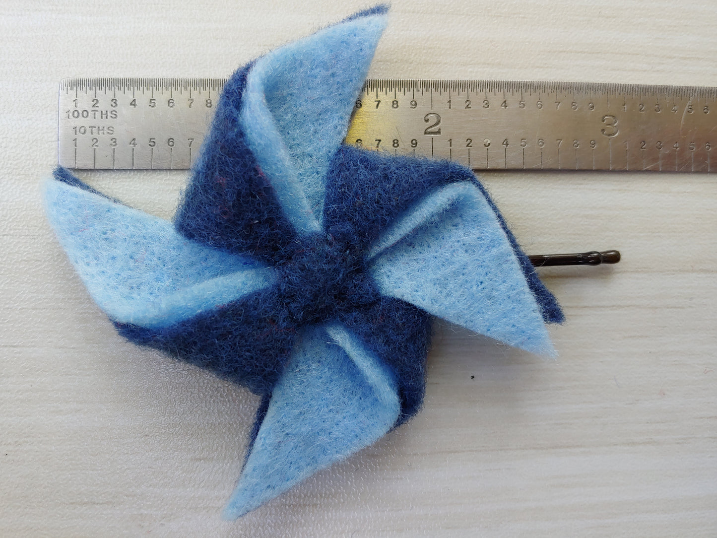 Handmade shades of blue pinwheel felt hair clip on a bobby pin, perfect for adding a pop of color and whimsy to any hairstyle. Hair clip next to ruler to show the size.
