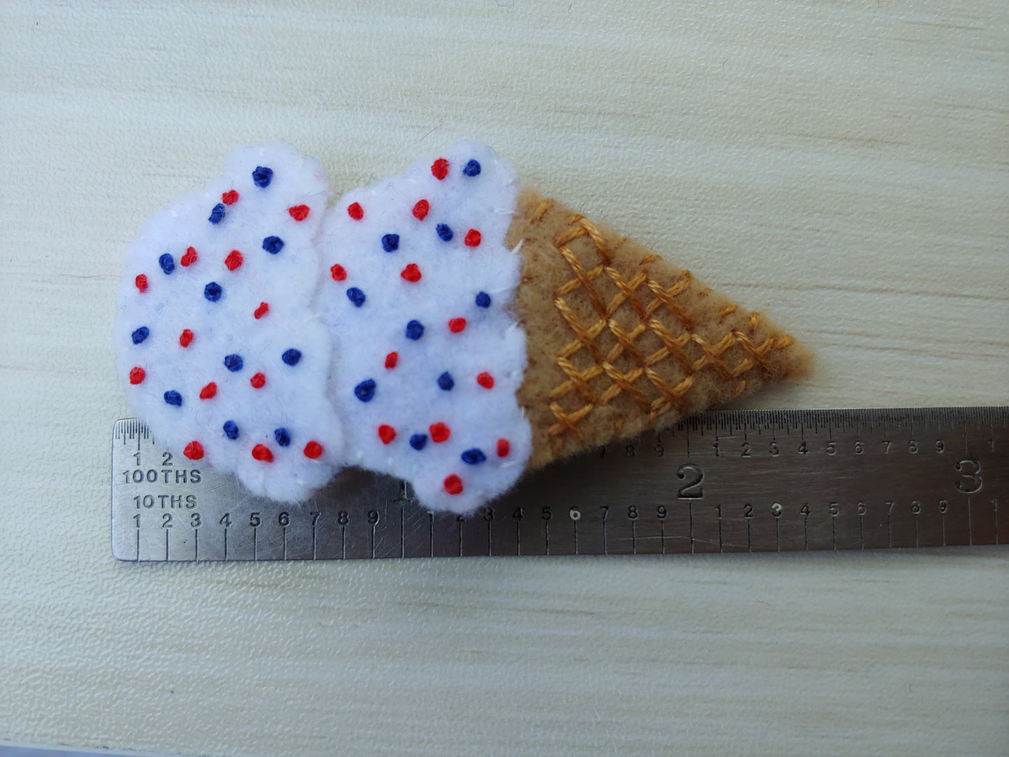 Handcrafted Patriotic Ice Cream Cone Felt Hair Clip featuring a tan cone, white scoops, and red & blue sprinkles on a secure snap clip - next to a ruler. A fun 4th of July accessory.