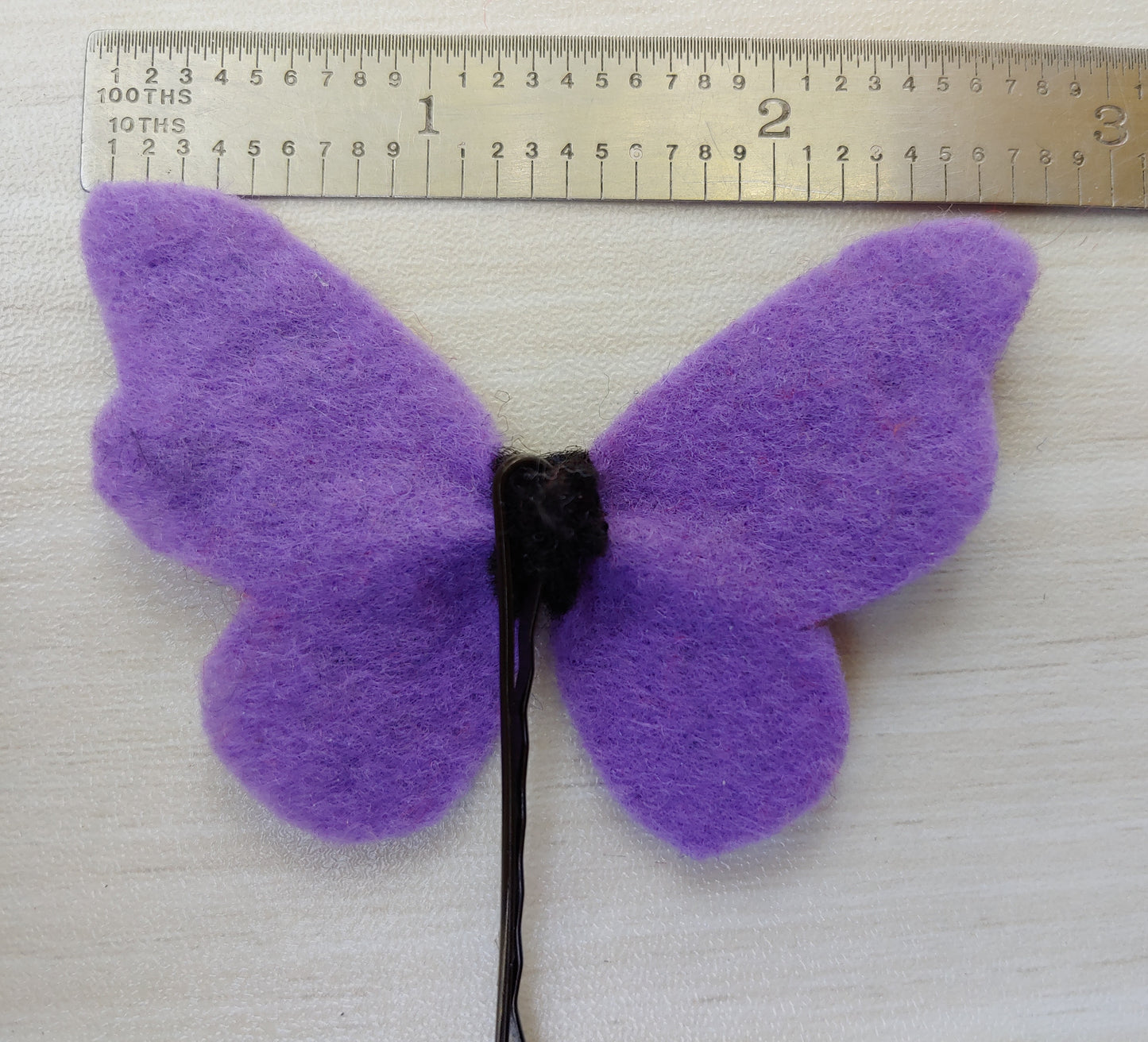 Handcrafted Purple Butterfly Felt Hair Clip featuring soft felt wings with black accents on a secure black bobby pin - reverse side, next to ruler. A whimsical hair accessory.