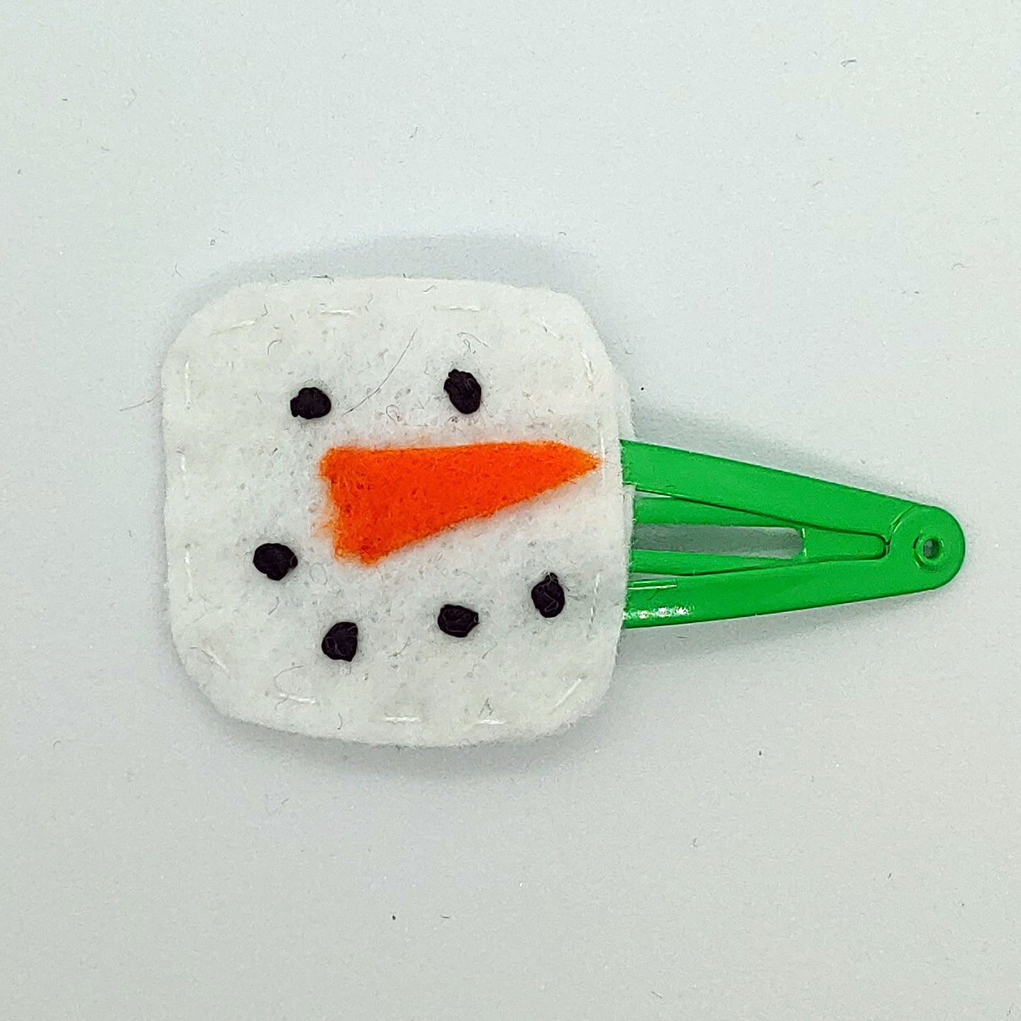 Handcrafted Snowman Felt Hair Clip featuring white felt, an orange nose, black embroidered details, and a snap clip. A fun winter accessory.