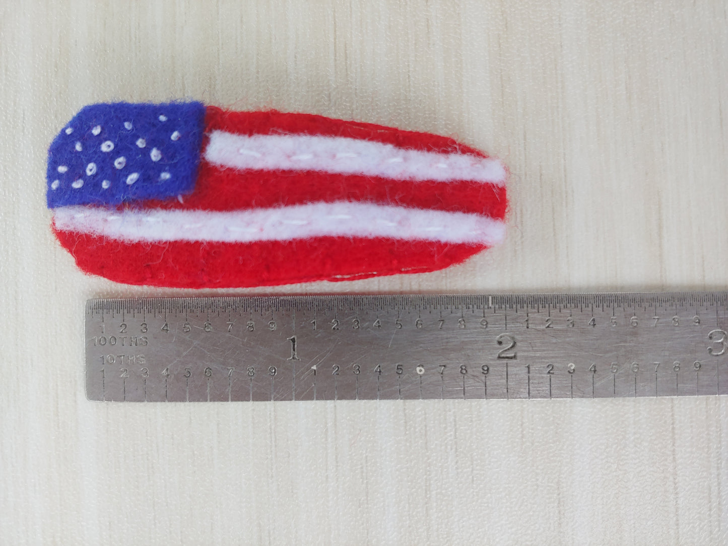 Handcrafted red, white, and blue patriotic flag felt hair clip on a metal snap clip next to ruler to show size. A festive accessory perfect for 4th of July & showing USA pride.