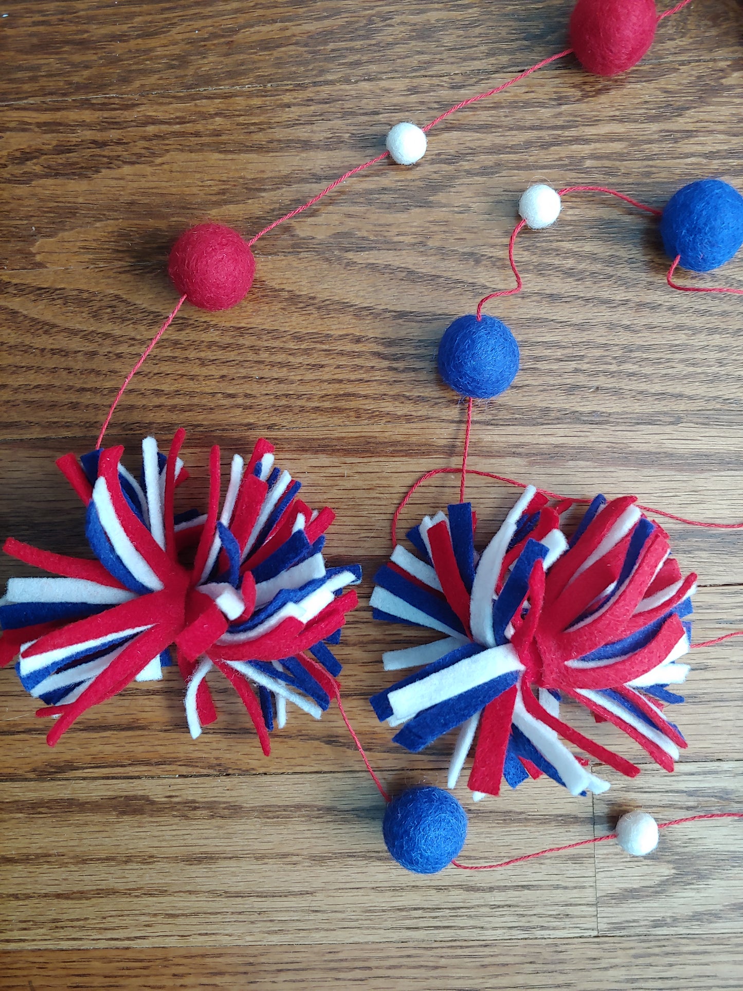 Handcrafted patriotic firework felt garland featuring red, white & blue felt fireworks and wool balls on craft twine. Perfect for 4th of July decor.