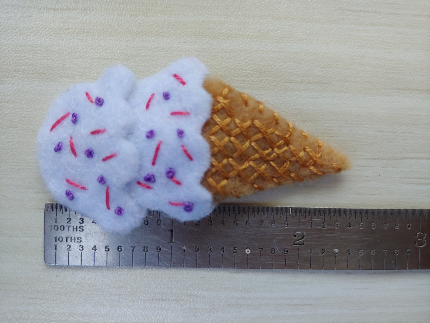 Handcrafted White Ice Cream Cone Felt Hair Clip featuring a tan cone, white scoops, and colorful sprinkles on a secure snap clip next to a ruler that indicates 2.5" tall. A fun, sweet accessory.