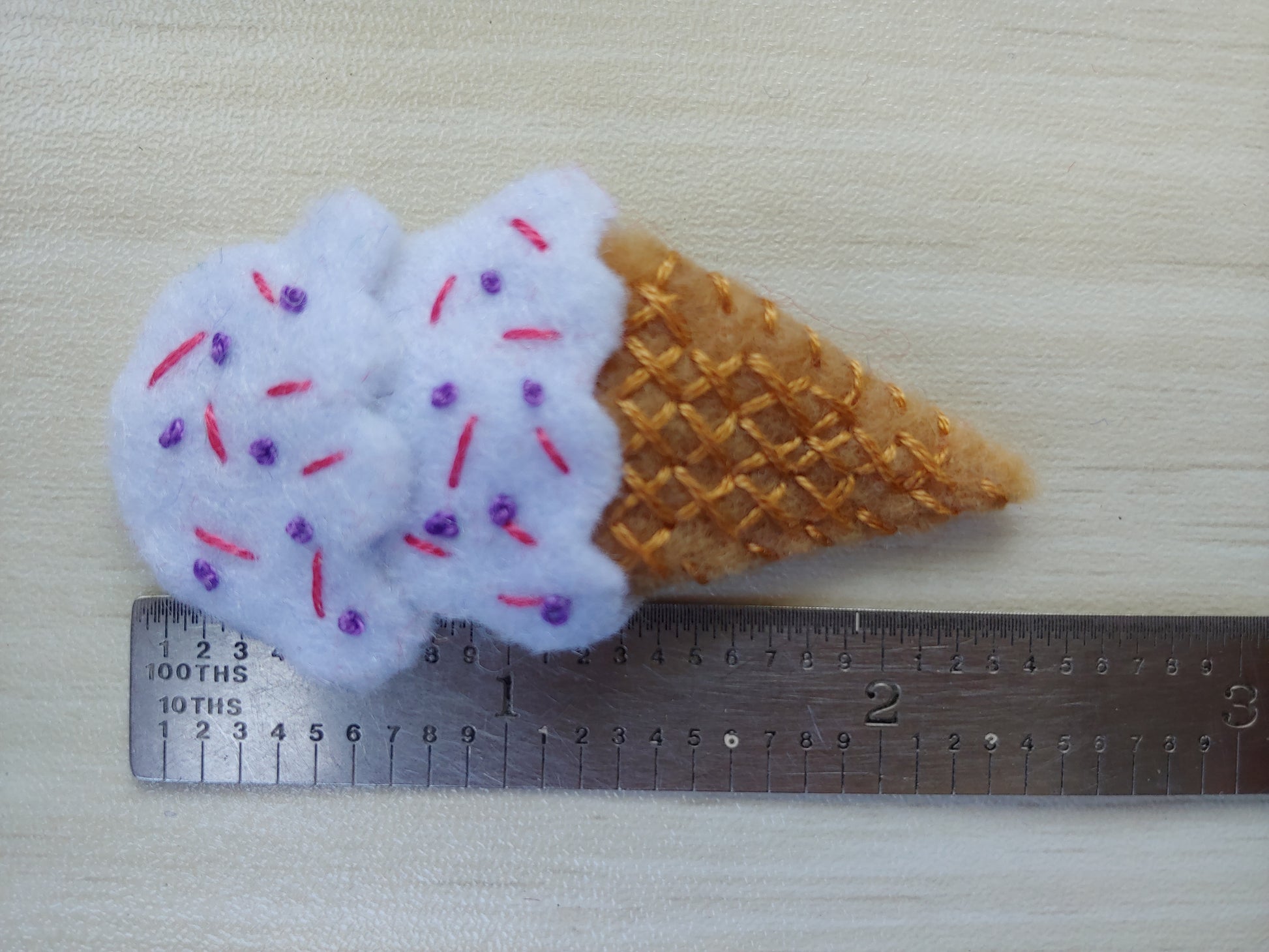 Handcrafted White Ice Cream Cone Felt Hair Clip featuring a tan cone, white scoops, and colorful sprinkles on a secure snap clip next to a ruler that indicates 2.5" tall. A fun, sweet accessory.
