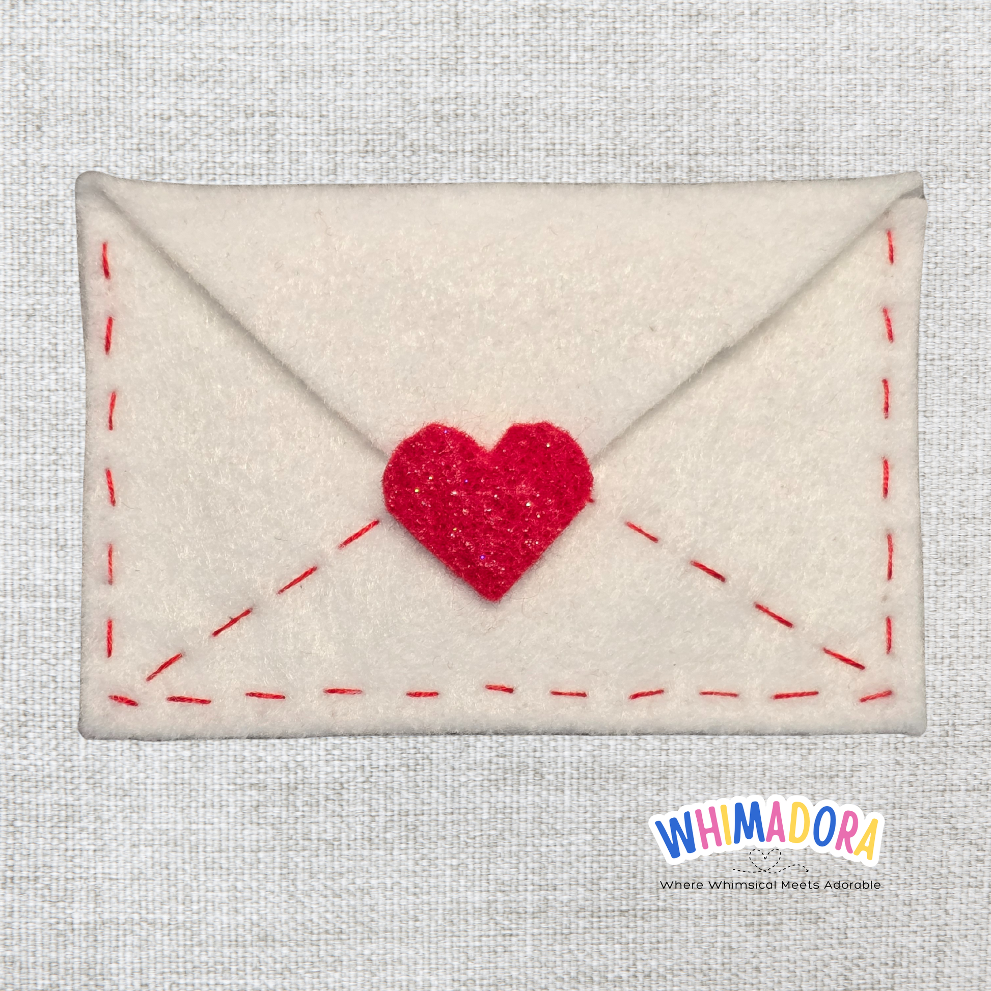 Envelope-shaped pouch with a red heart on a textured gray background, branded 'WHIMADORA'.
