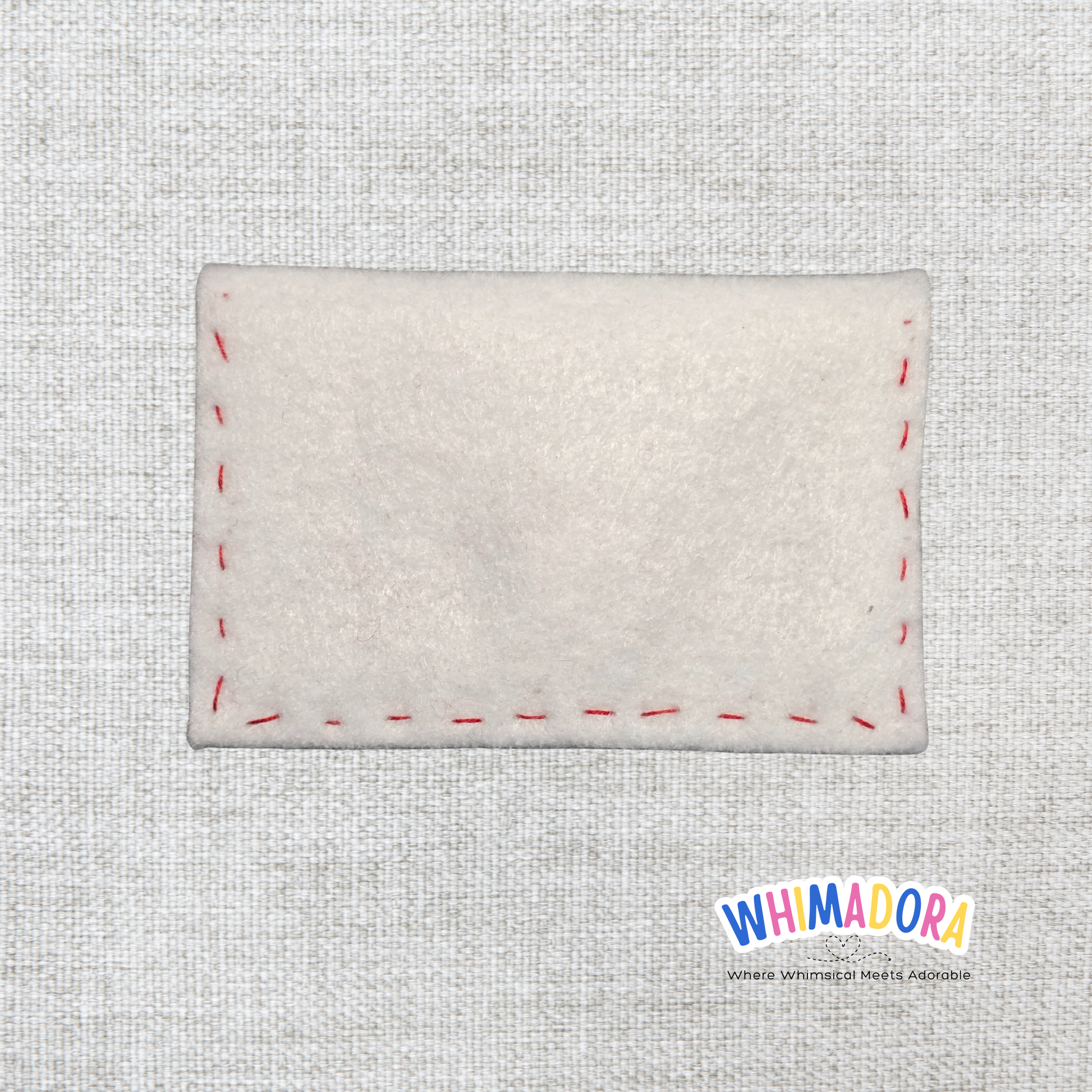Rectangular white felt patch with red stitching on a textured gray background, featuring the Whimadora brand.