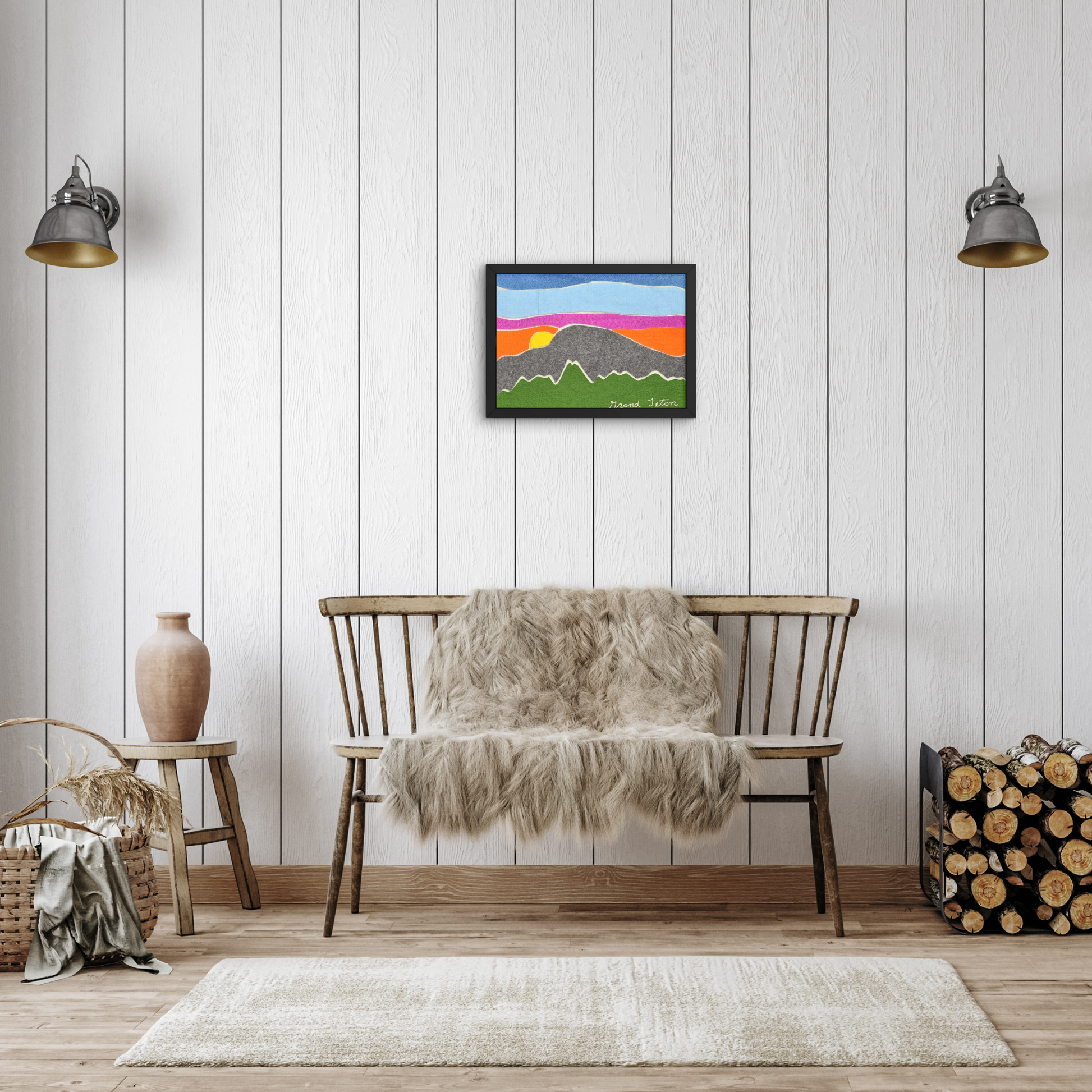 Framed Grand Teton felt wall art displayed in a cozy, modern rustic living space. The artwork hangs on a white wood-paneled wall above a bench with a faux fur throw. The room includes minimal décor like a ceramic vase, a wicker basket, and a firewood stack, highlighting a warm and inviting atmosphere.