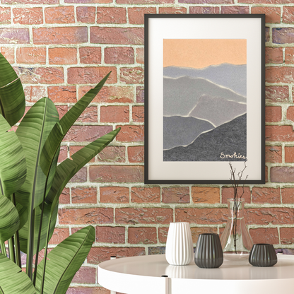 Abstract Smoky Mountain wall art in black frame on a brick wall with a plant to the left of the art. White topped table with 4 vases on it below the art.