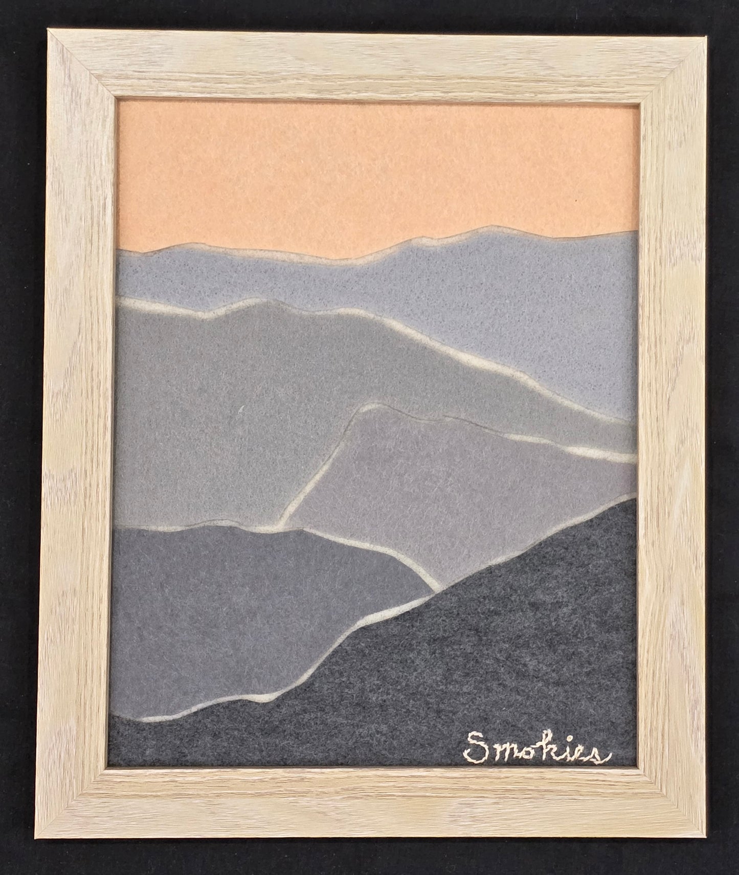 Abstract felt layered to look like "smoky" mountains in a neutral wood frame on a black background.