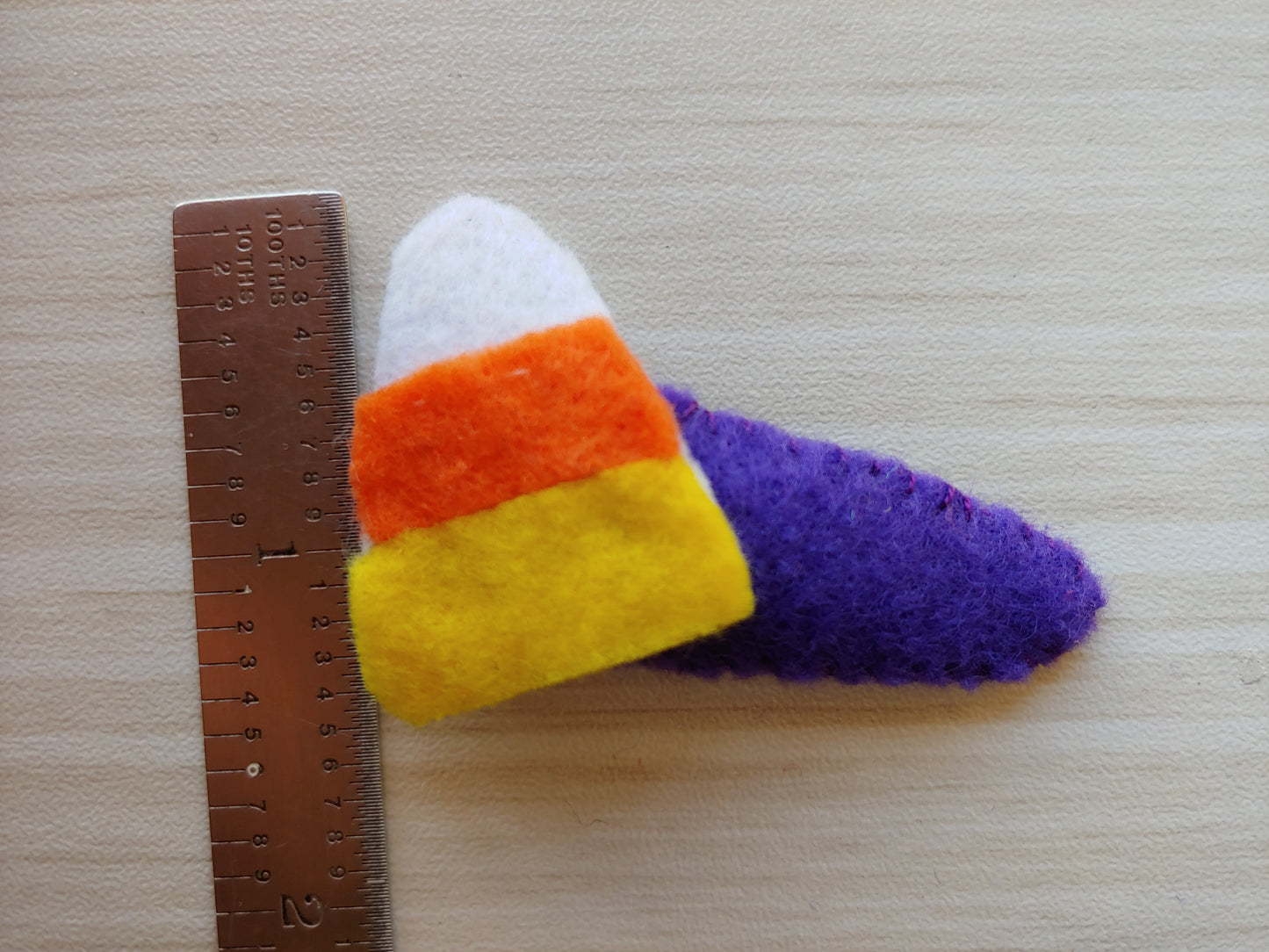 Candy Corn shaped cutout attached to snap clip covered in purple felt. Scales 14 tenths tall.