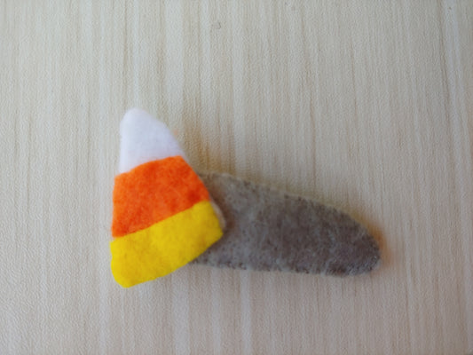 Candy Corn shaped felt attached to snap clip covered in gray felt. 