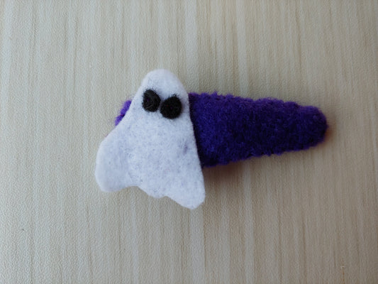White Ghost cut out of felt with black felt eyes. Ghost stitched onto a snap clipped covered in purple felt.
