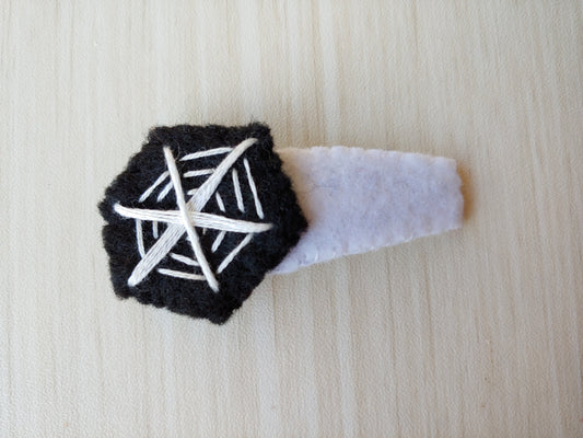 Black felt cut to hexagon shape with white lines stitched on to create spiderweb effect. Attached to snap clip covered in white felt.